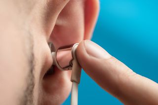 To get the best headphones for cycling to fit you need to insert it correctly. This image is a close up of an ear on the left side, with a finger inserting a headphone close up.